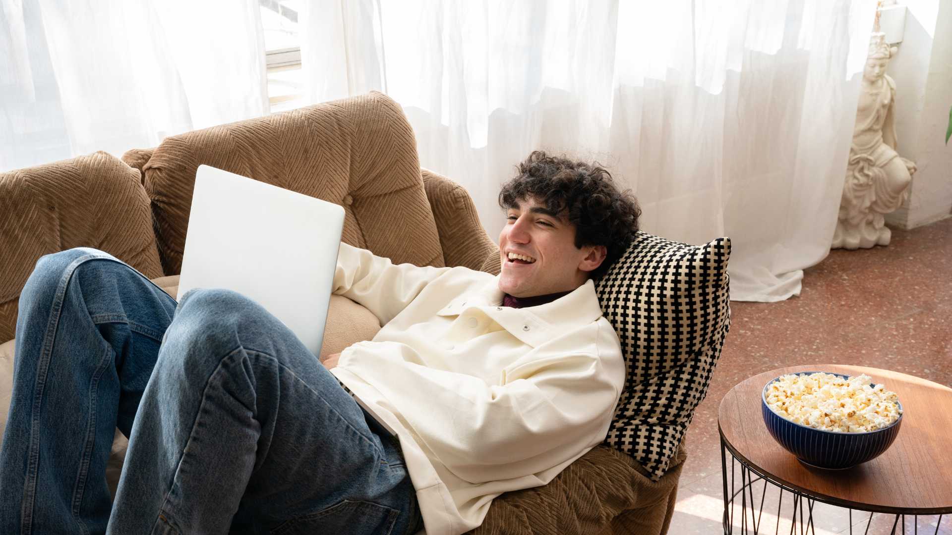 Jeune homme qui regarde une série sur son ordinateur portable posé dans son canapé 